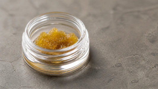 Golden live resin sugar with a wet granular texture in a clear glass jar.
