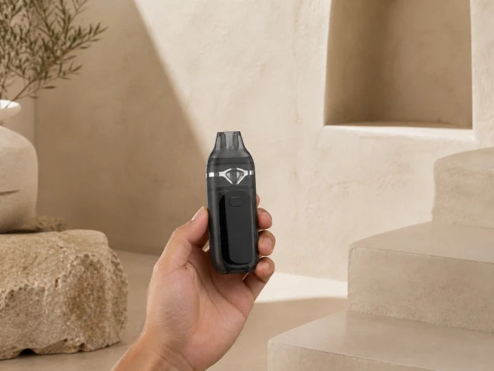 Black Lumen dual-chamber empty AIO held upright from the sides with its display powered off in a warm ivory studio